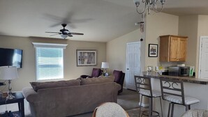 A living room with a sofa, a ceiling fan, a TV, and a dining area with a table and chairs. - Lake Roosevelt View Retreat Grand Coulee (Grand Coulee)