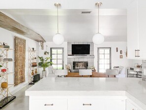 A spacious living room with a large white island, a fireplace, and a flat-screen TV. - Boho(asis) - Incredible Views, Dog Friendly, Quiet (La Quinta)