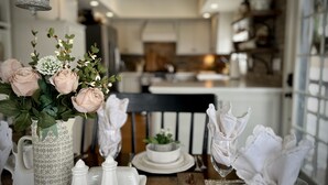 Una mesa de comedor dispuesta con vajilla blanca, un florero con rosas rosadas y una mesa de madera rústica.