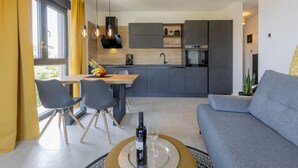 Eine moderne Küche mit grauen Schränken, eine Essecke mit einem Holztisch und Stühlen sowie ein graues Sofa.