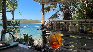 Eine Strandbar mit Meerblick, ein Getränk auf der Theke und verschiedene Alkoholflaschen.
