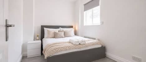 A minimalist bedroom with a bed, bedside table, and a window.
