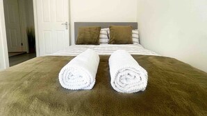 A hotel room with a bed, two pillows, and two rolled towels on the bed.