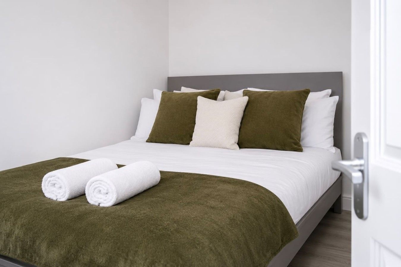 A neatly made bed with white bedding and green accents, including pillows and a blanket.
