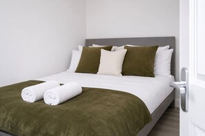 Ein ordentlich bezogenes Bett mit weißer Bettwäsche und grünen Akzenten, darunter Kissen und eine Decke.