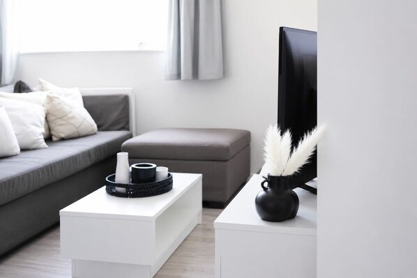 A modern living room with a grey sofa, a white coffee table, and a black TV stand.