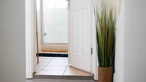 A hallway with a white door leading to a room with a tiled floor and a wooden bench.