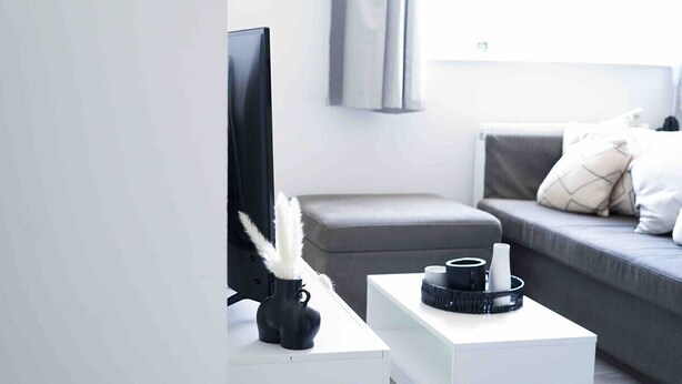 A modern living room with a flat-screen TV, a white coffee table, a grey sofa, and a grey ottoman.