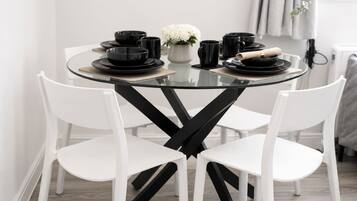 A round glass table with black and white chairs, black plates, cups, and a vase with white flowers.