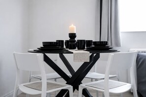 Una mesa de comedor con vajilla negra y una vela, rodeada de sillas blancas.