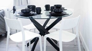 A modern dining area with a glass table, white chairs, and black tableware.