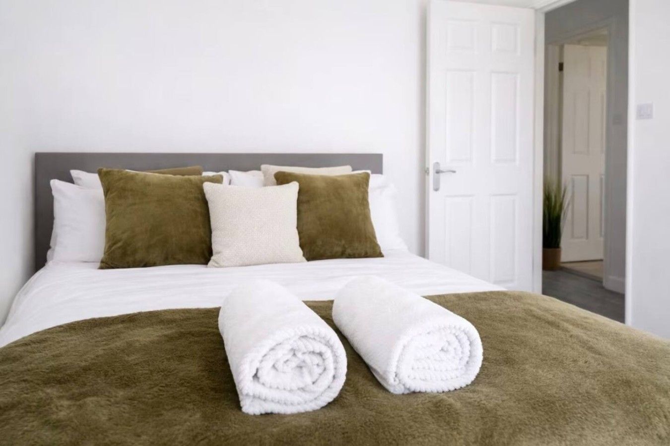 A neatly made bed with a white duvet, two rolled white towels, and a brown throw blanket.