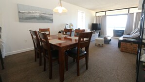 Un coin repas avec une table et des chaises en bois, un tableau au mur et un téléviseur dans le salon.