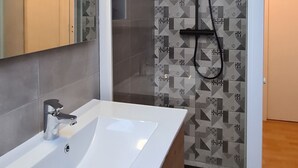 A modern bathroom with a white sink, a glass shower enclosure, and patterned tiles. - Fully renovated house, garden & terrace 5mn from the beach, underfloor heating (Combrit)
