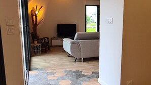 Un saló modern amb terres de fusta, un sofà, una televisió i un arbre decoratiu.