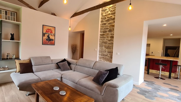 A modern living room with a grey sectional sofa, a wooden coffee table, and a stone accent wall. - Fully renovated house, garden & terrace 5mn from the beach, underfloor heating (Combrit)
