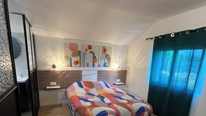 Un dormitori amb un llit, una taula de nit, una làmpada, una paret amb art abstracte i una finestra amb cortines.