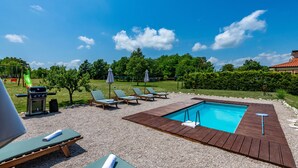 Un espace piscine doté d’une terrasse en bois, de chaises longues et d’un barbecue.