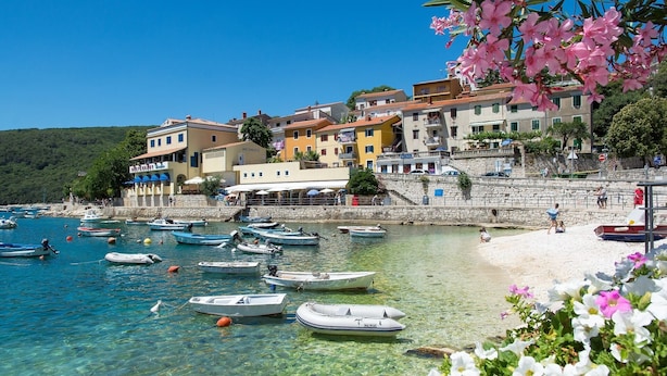 Une ville côtière aux eaux cristallines, où les bateaux sont amarrés le long de la plage et où les bâtiments arborent des couleurs vives.