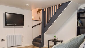 A modern living room with a flat-screen TV, a staircase, a radiator, and a bookshelf. - 2 bedroom accommodation in Street (Street)