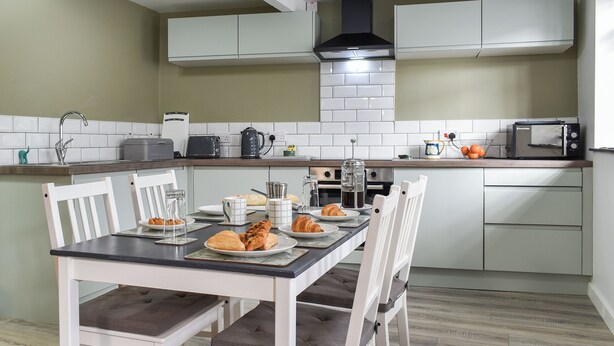 A modern kitchen with white cabinets, a dining table with chairs, and a built-in oven. - 2 bedroom accommodation in Street (Street)