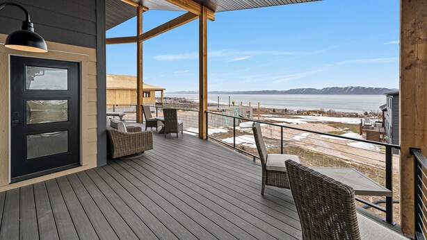 A wooden deck with wicker furniture, a black door, and a view of a body of water and mountains. - Highland Chateau at Longridge  (Sleeps 34) (Garden City)