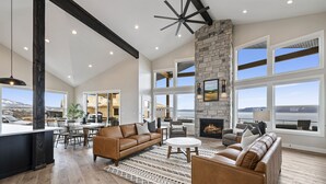A spacious living area with a fireplace, large windows, and a high ceiling with exposed beams. - Highland Chateau at Longridge  (Sleeps 34) (Garden City)