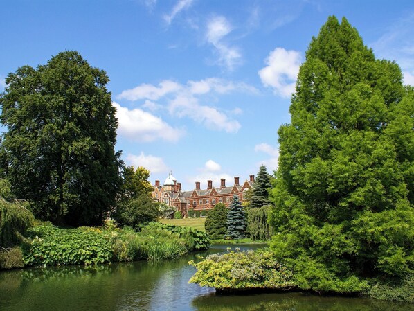 A large, historic building with a symmetrical facade, surrounded by lush greenery and a calm water feature.