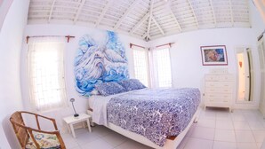 A bedroom with a large bed, a chair, a nightstand, a dresser, and a painting on the wall. - One Rythm (Duncans)