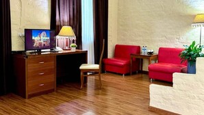 A hotel room with a wooden desk, a television displaying a hotel image, a red sofa, a small table with a lamp, and a potted plant. - RETRO PALACE (Tashkent)