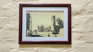 A framed historical photograph of a building with a tower and arches, mounted on a textured wall. - RETRO PALACE (Tashkent)