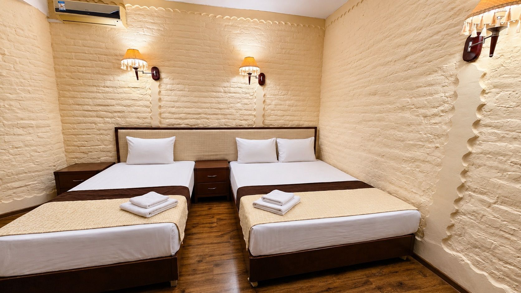 Une chambre d’hôtel avec deux lits, un plancher en bois et un mur en briques.