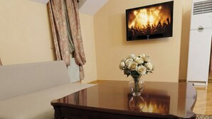 Una habitación con sofá, una mesa de centro de madera con un florero y un televisor de pantalla plana en la pared, además de un radiador.