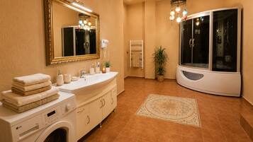 A bathroom with a washing machine, a sink with a mirror, a towel stack, a potted plant, and a shower enclosure.