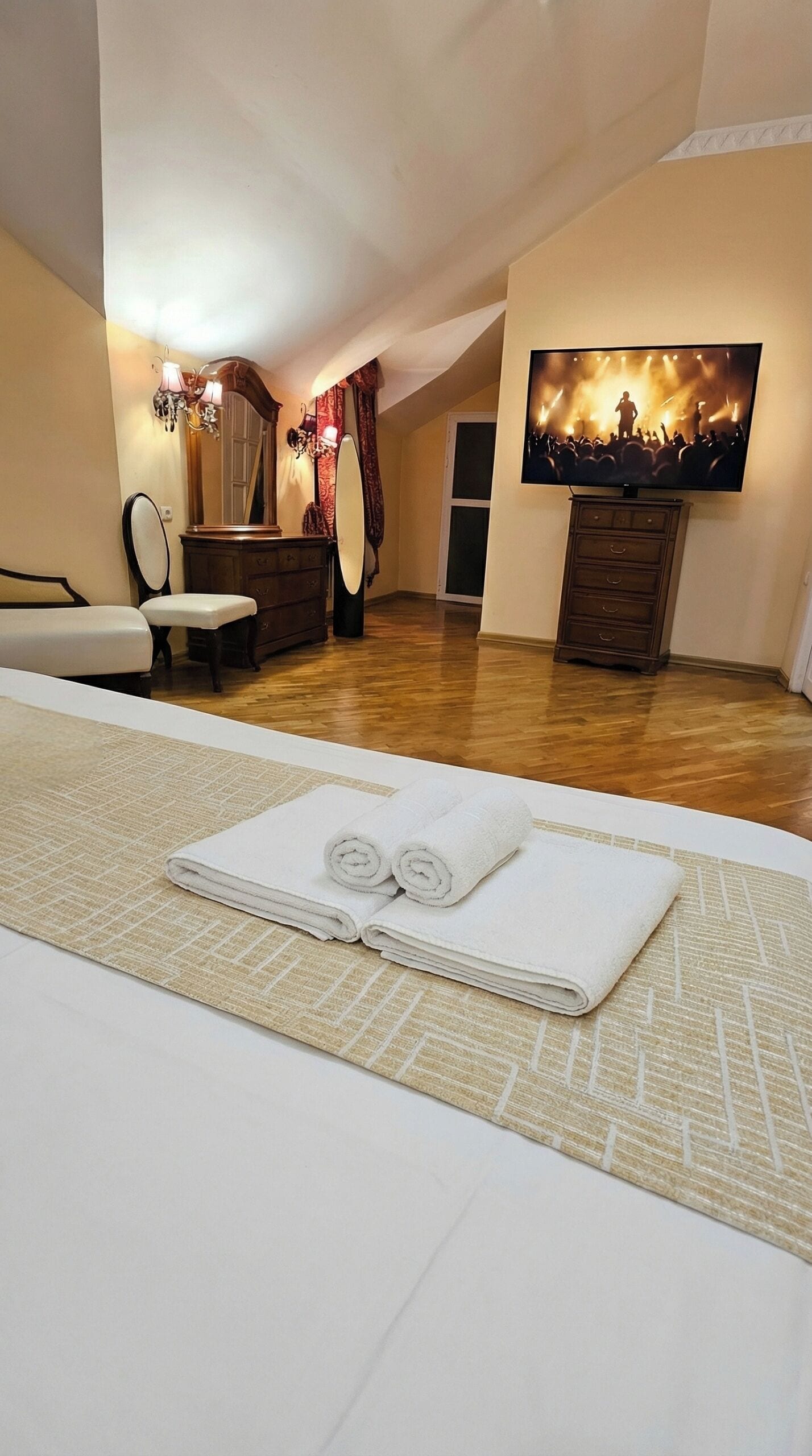 A hotel room with a bed, a large mirror, a dresser, a television, and a painting on the wall.
