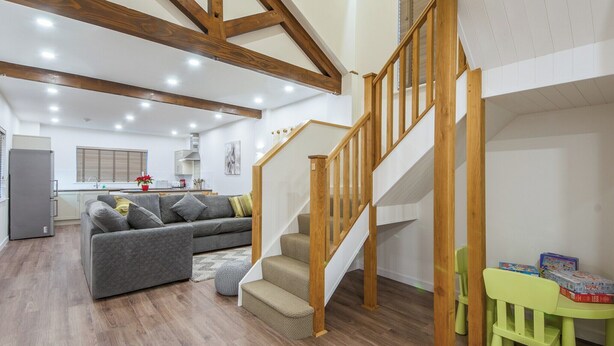 A spacious living area with a wooden staircase, a grey sofa, and a children's table with toys. - Fir Cottage - UK38485 (Saltash)