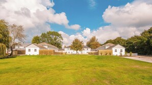 A row of white houses with solar panels, surrounded by a grassy field and trees under a partly cloudy sky. - Fir Cottage - UK38485 (Saltash)