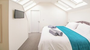 A bedroom with a bed, a TV mounted on the wall, and skylights. - Fir Cottage - UK38485 (Saltash)
