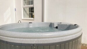 A hot tub with a stone exterior and a wooden base, positioned against a white wall with a window. - Fir Cottage - UK38485 (Saltash)