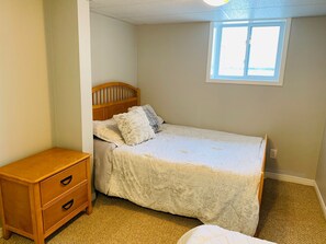 Ein Schlafzimmer mit einem Einzelbett, einem Nachttisch aus Holz mit Schubladen, einem Fenster und einem Teppichboden.