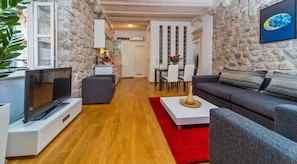 A cozy living room with a stone wall, a flat-screen TV, a grey sofa, and a red rug.