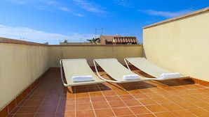Une terrasse sur le toit avec trois chaises longues, un sol carrelé et un ciel bleu dégagé.