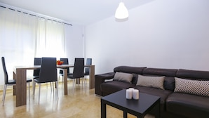 Un salon moderne avec un canapé marron foncé, une petite table noire ornée de bougies et un coin repas comprenant une table en bois et des chaises noires.