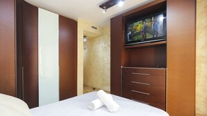 Une chambre d’hôtel avec un lit, un téléviseur fixé au mur, une armoire en bois et une salle de bain visible à travers une porte ouverte.
