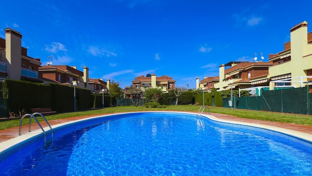 Une piscine à l’eau d’un bleu limpide, entourée d’une pelouse bien entretenue et bordée, au loin, par une rangée d’immeubles d’habitation.