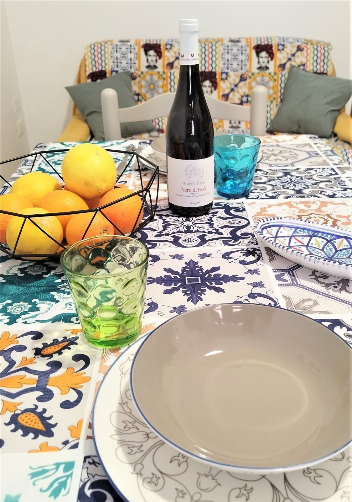 A table with a bottle of wine, a bowl, a glass with ice, and a basket of oranges.