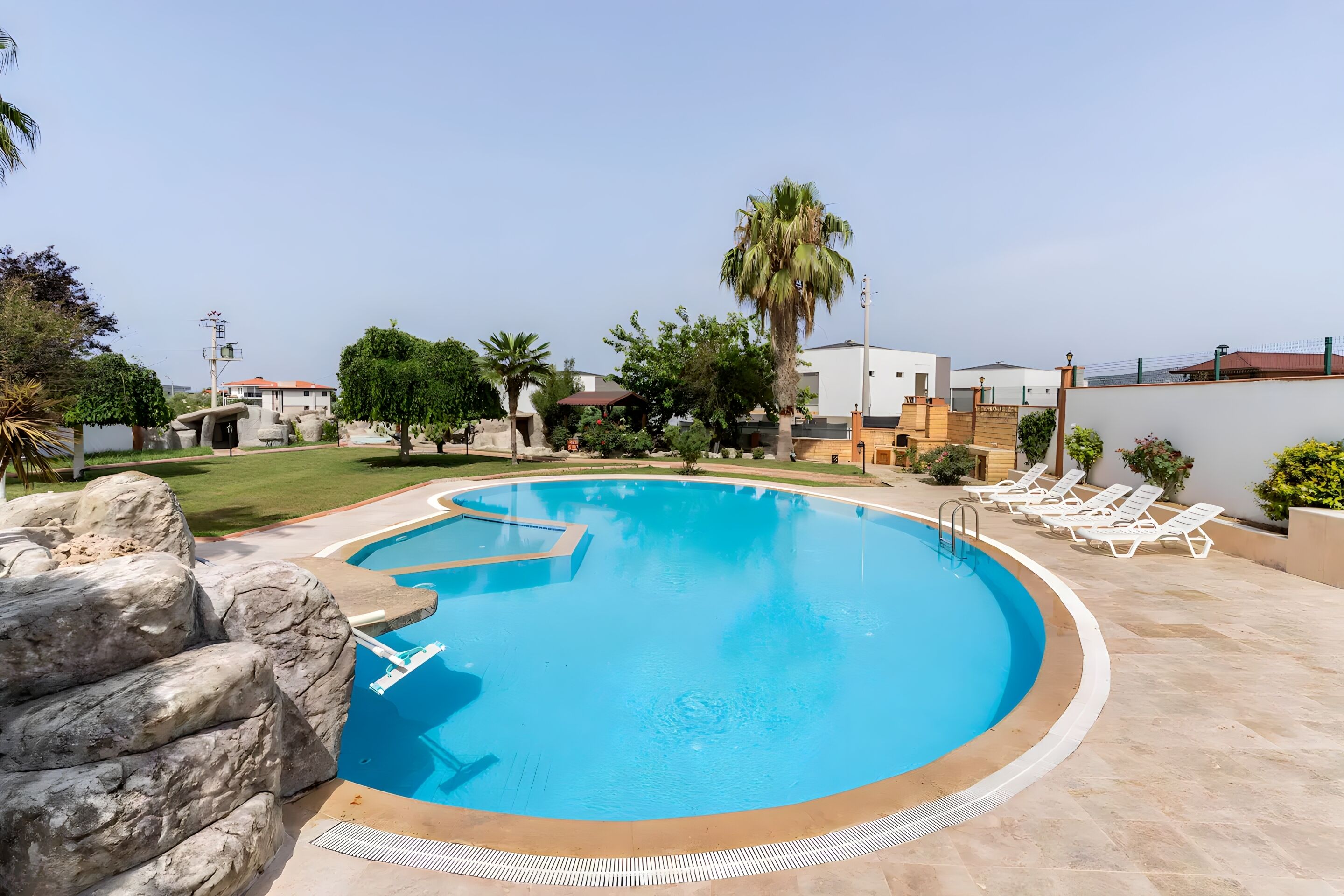 Una piscina con muro de piedra, sillas de descanso y palmeras.