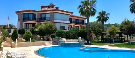 A multi-story building with a swimming pool, outdoor seating, and palm trees.