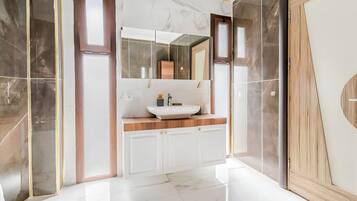 Un baño moderno con un espejo grande, un lavabo blanco y suelo de mármol.