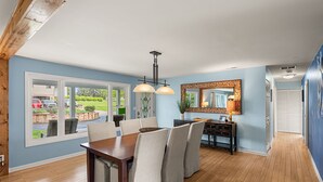 A dining area with a wooden table and chairs, a chandelier, and a large window with a view of the outside.